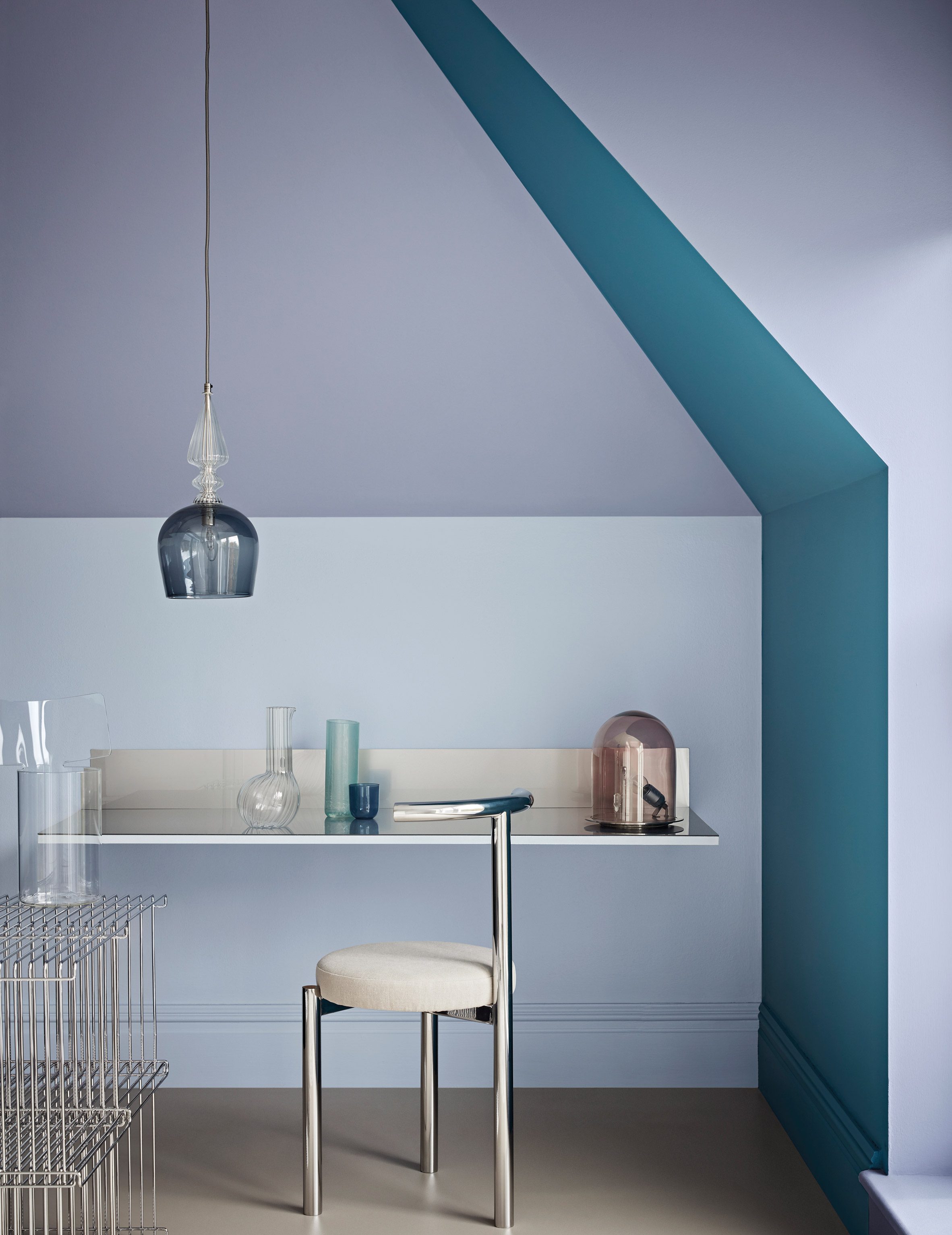 Desk nook with transparent, crystal-like objects and metal furniture against pale blue, grey and teal walls