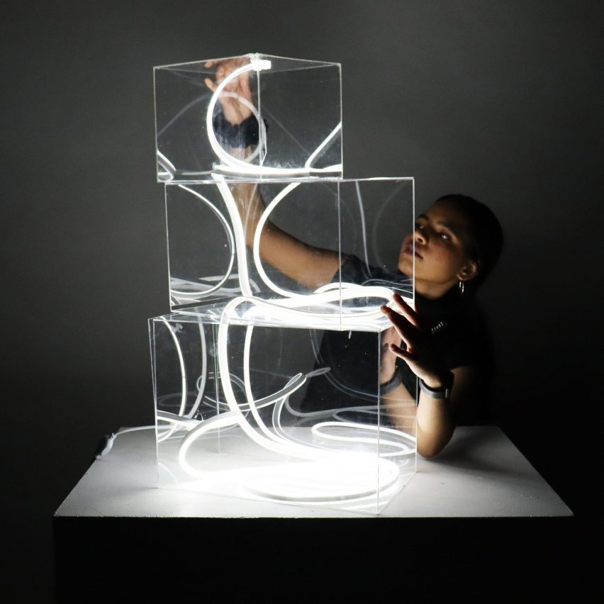 A person holds three stacked clear boxes containing illuminated ribbons on a podium