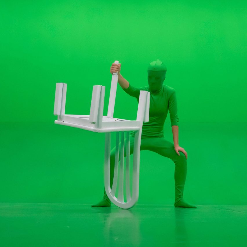 Green suited figure holds a white lawn chair in front of a green screen