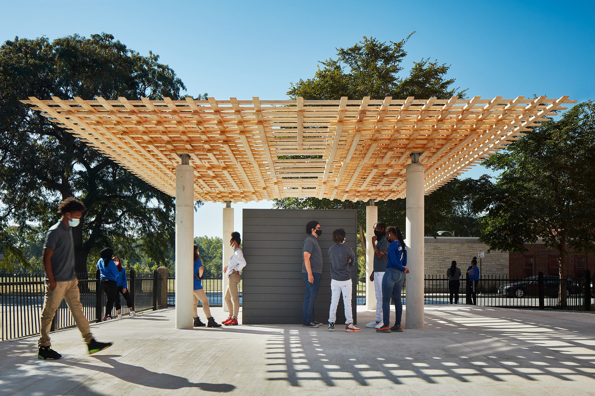 Students stand under the interlocking timber roof of the SPLAM pavilion