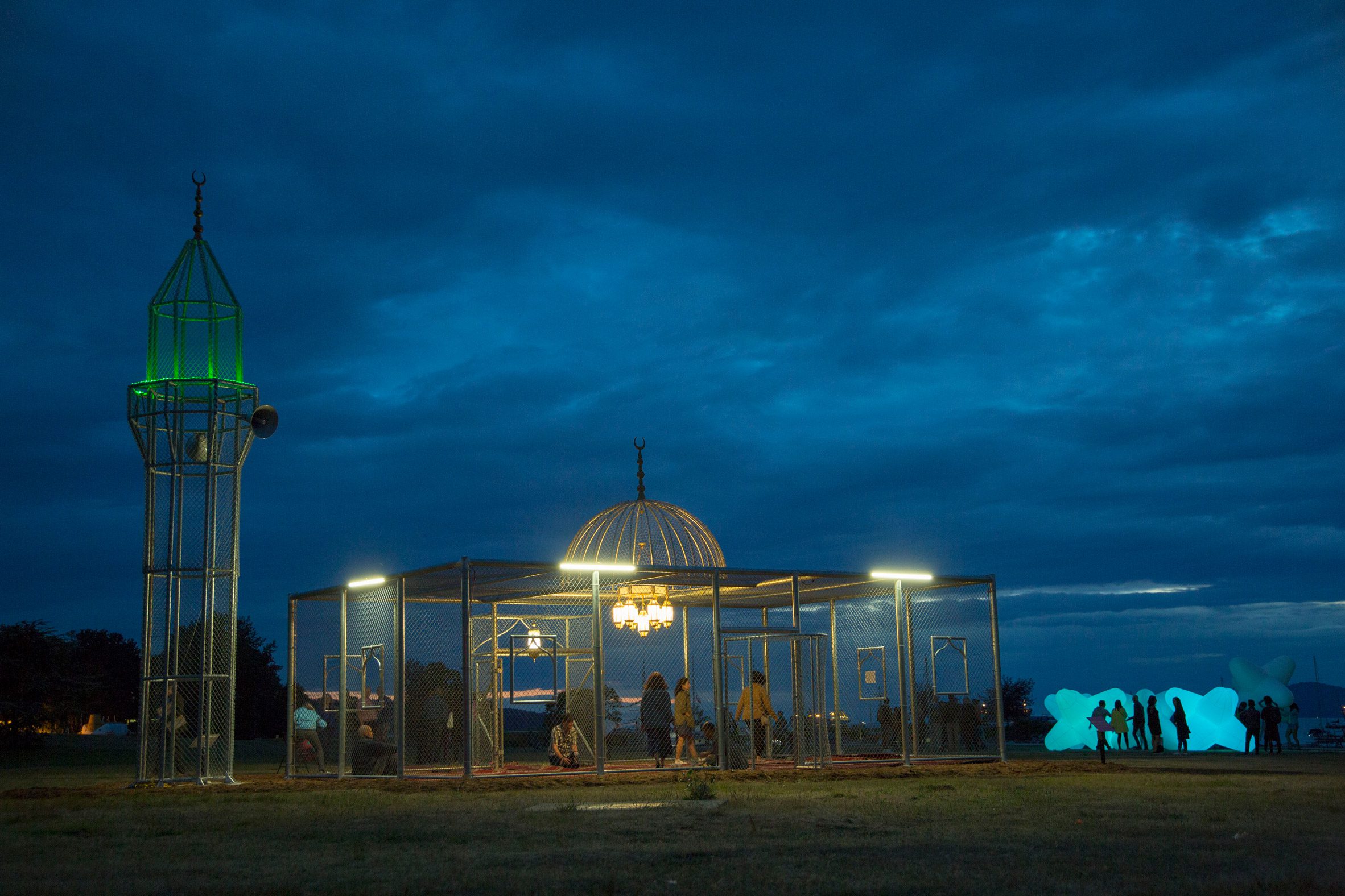 The steel mosque installation at dusk, with the minaret lit in green