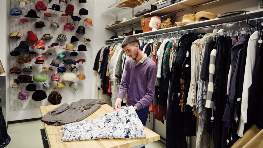 Man cuts fabric in fabric store with hats on wall