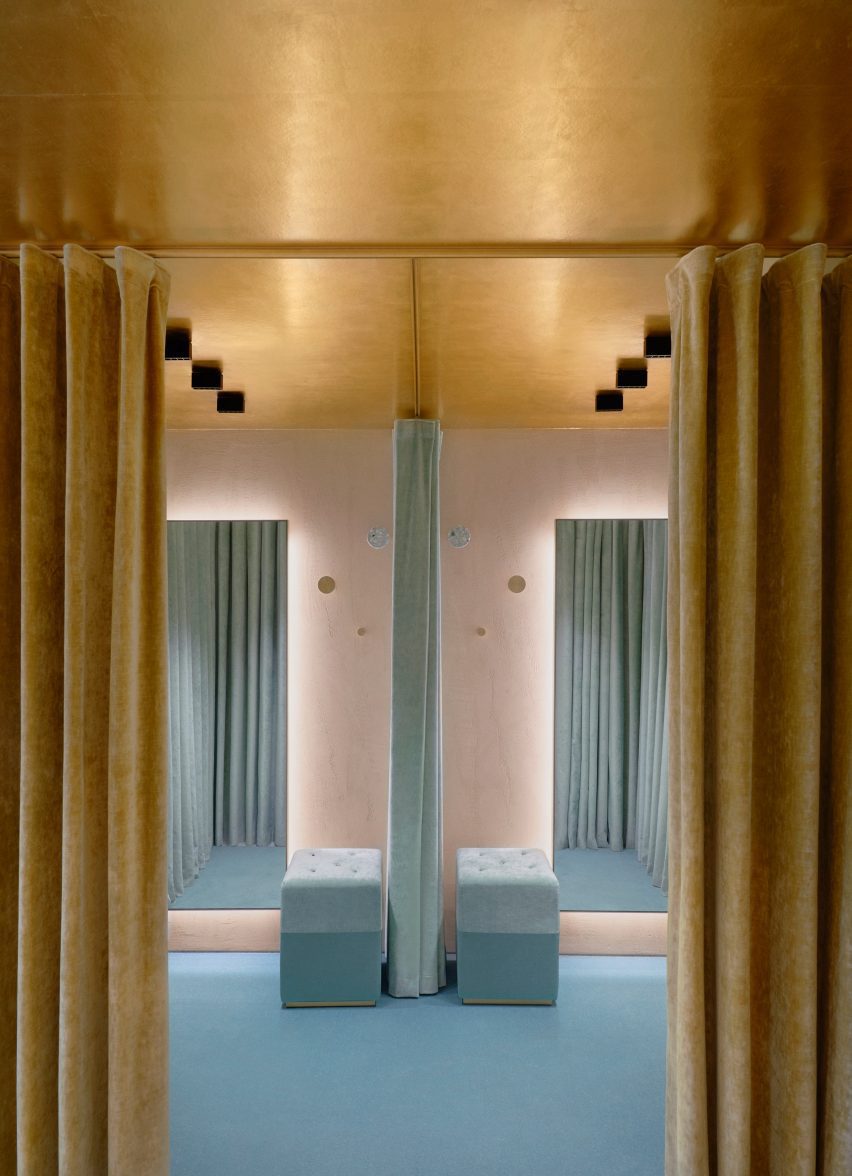 Ruang ganti dengan lantai biru muda dan tirai beludru emas di ruang ritel Forte dei Marmi