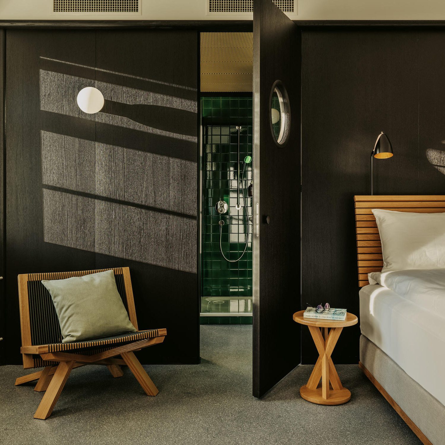 Bedroom with wooden furnishings looking into a green-tiled bathroom
