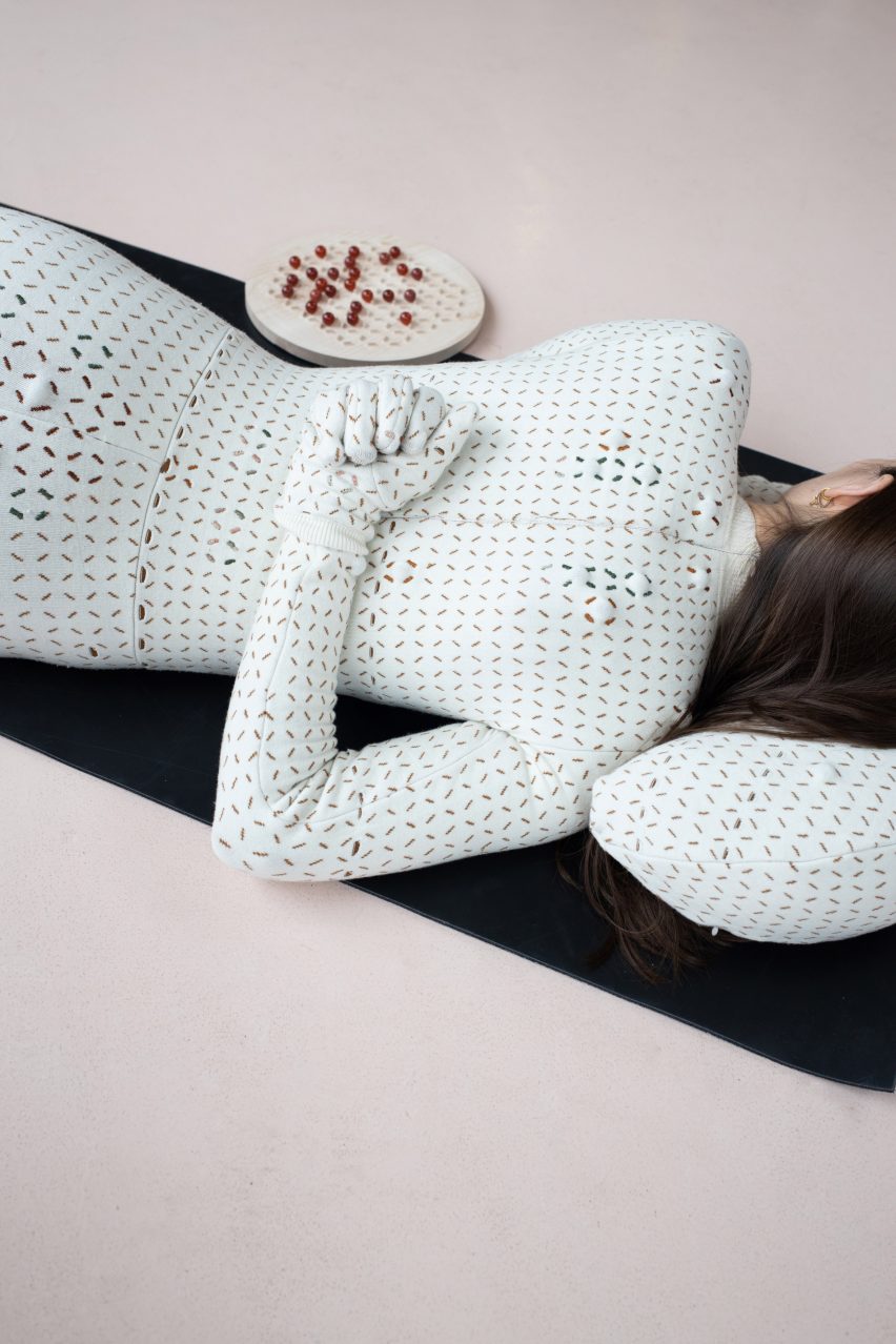 A woman is lying on a yoga mat on her stomach with her head resting on a therapeutic pillow