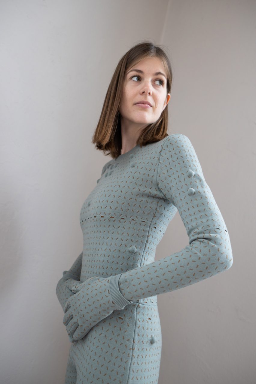 Woman wearing light teal bodysuit with matching gloves with stitched grid pattern and massage balls inside grid