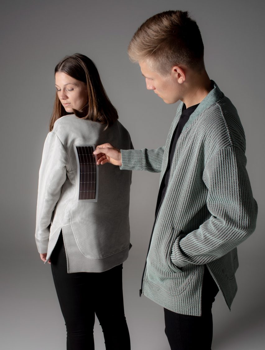 One person holds a solar cell strip up against the back of another person wearing a light grey jacket