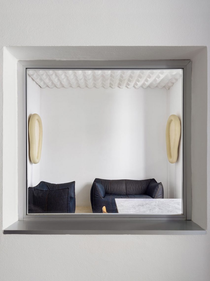 A squared window looks into a room with sofas and chairs