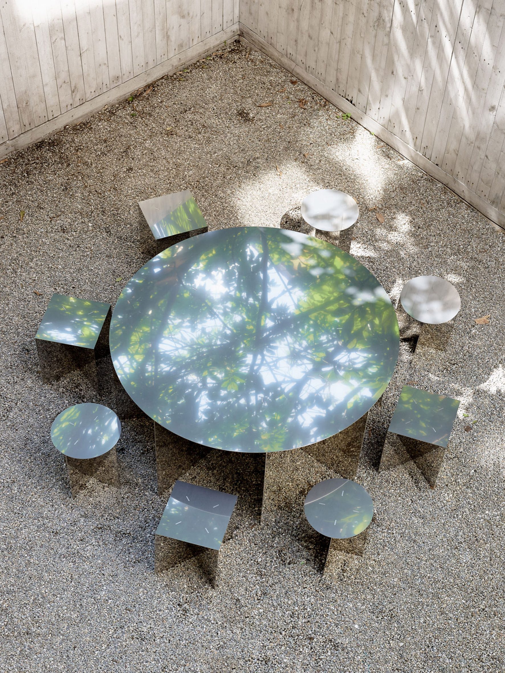 A metal table and chair reflects the trees and shrubbery