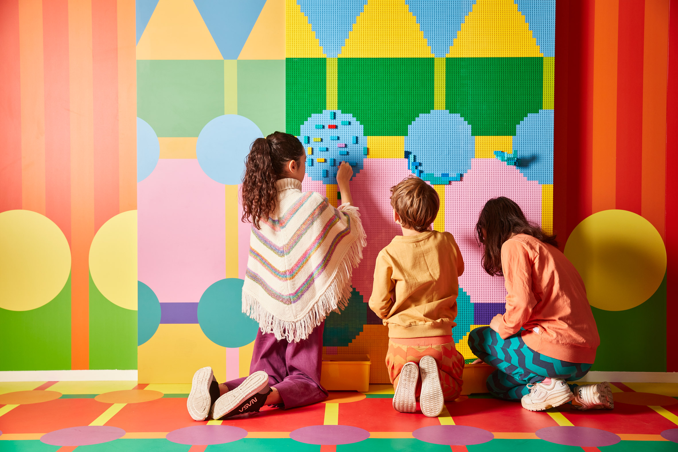 Kids add Lego bricks to a wall mural in the Laundrette of Dreams