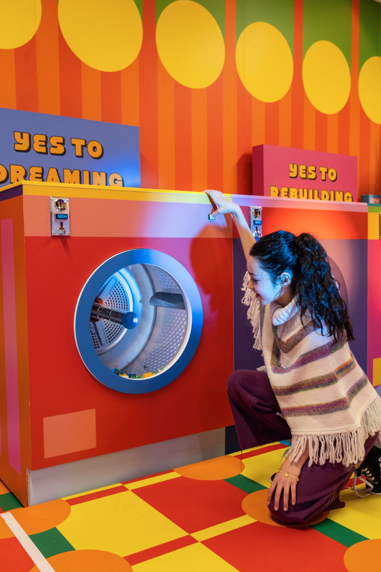 Child stares into a colourful washing machine drum at the Lego laundrette