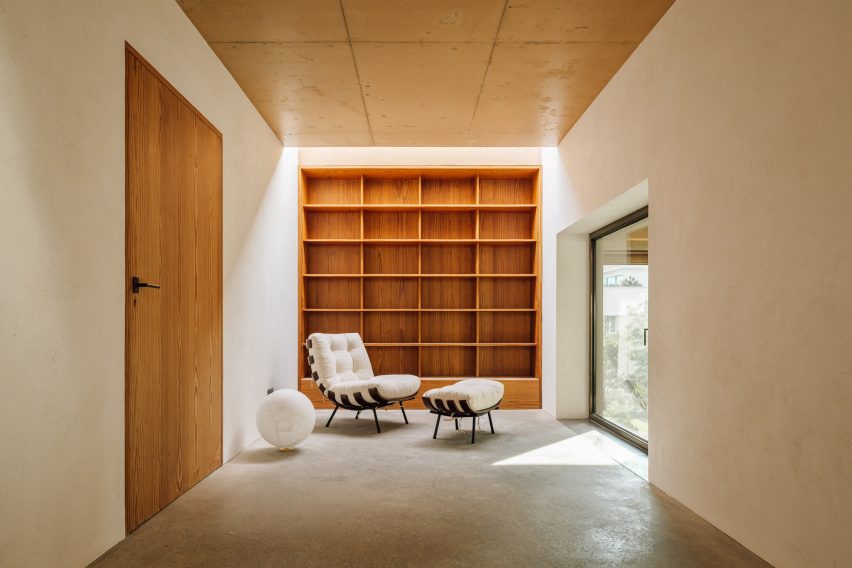 Tampilan interior ruang belajar di Casa 2 Porto dengan rak kayu built-in dan kursi santai putih