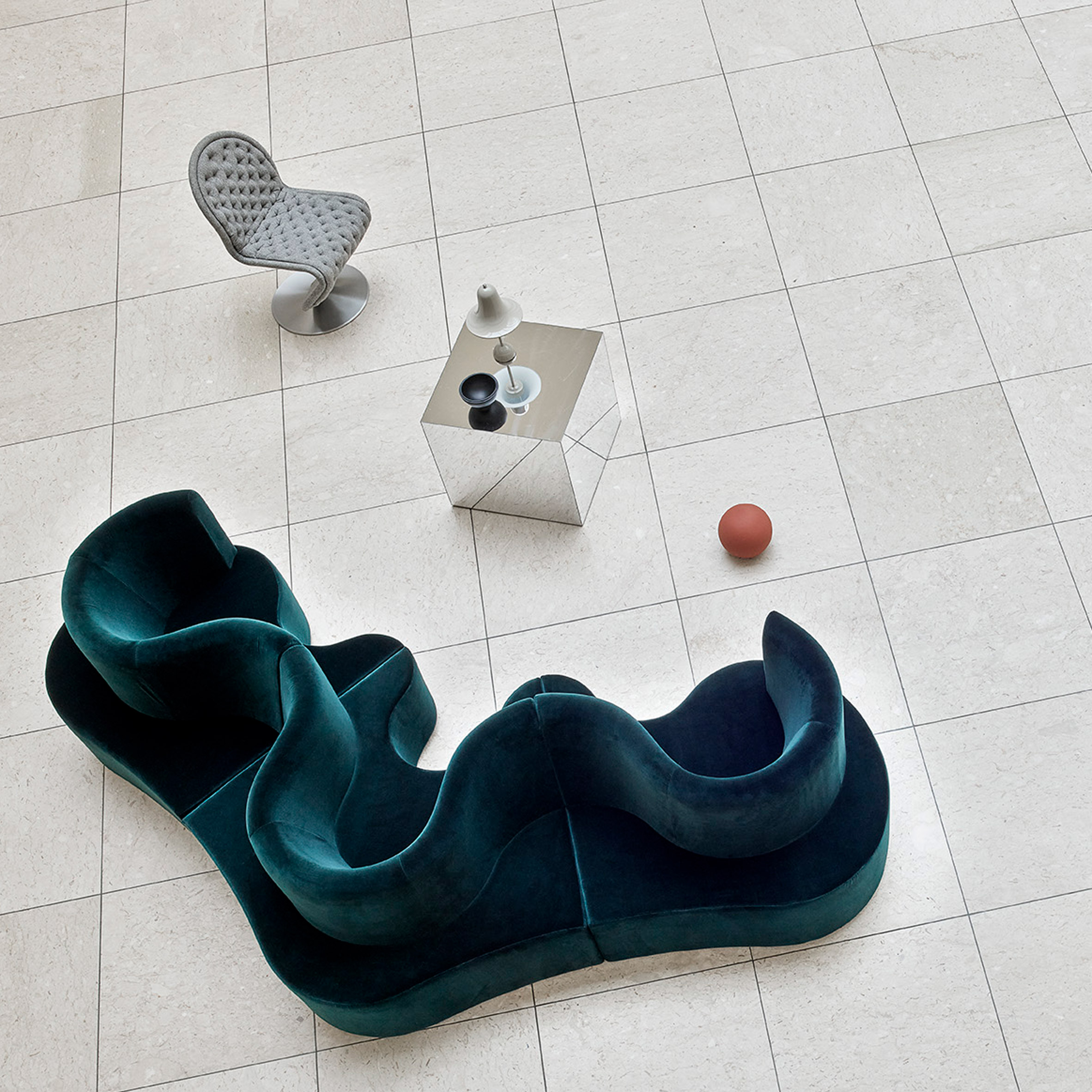 A photograph taken from above of a green velvet Cloverleaf sofa on a white tiled floor, showing its curved form