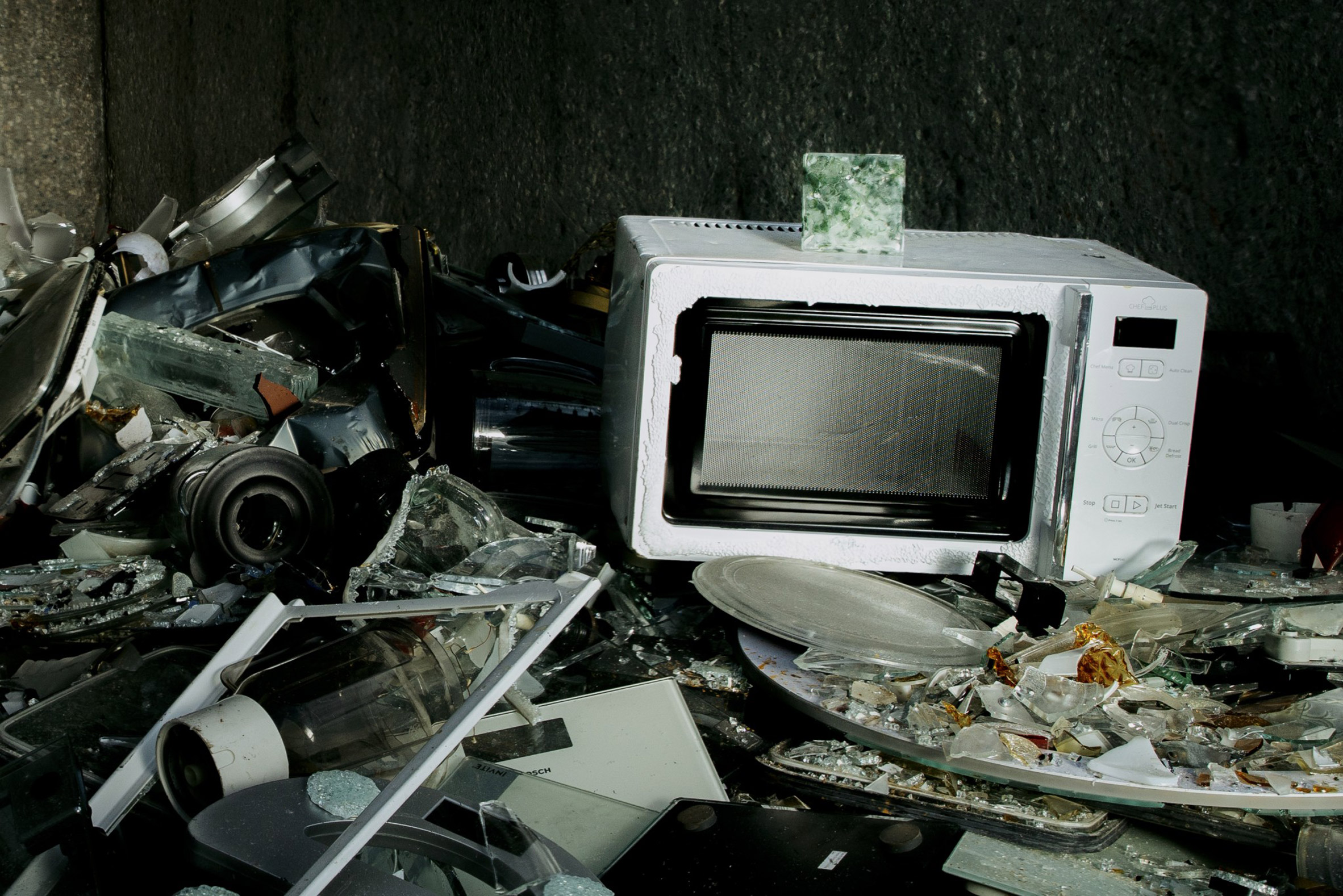 A Common Sands tile sitting on top of a microwave in a pile of broken glass and e-waste