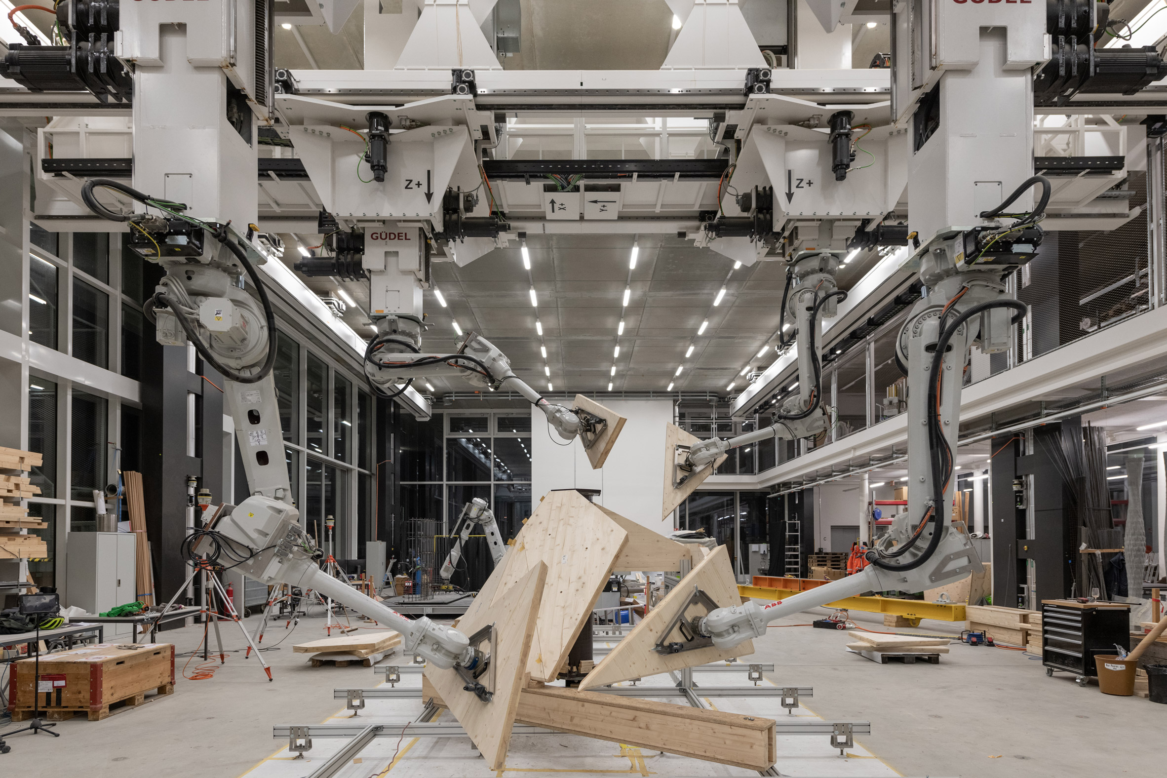 Robot arms move through the air holding wooden panels in a manufacturing centre