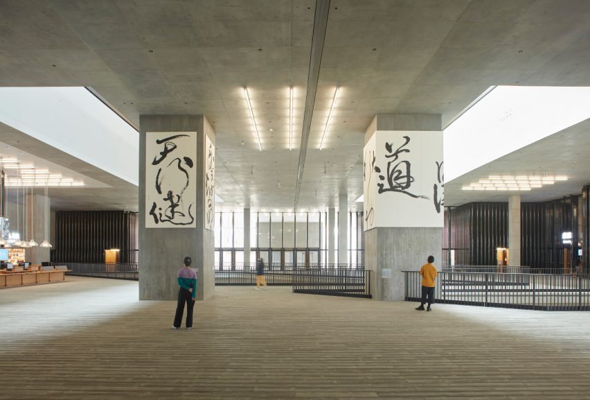 Aula utama Museum M+ dengan kolom beton struktural yang menampilkan karya seni kaligrafi