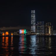 M+ museum with its facade illuminated at nighttime with the light reflecting on Victoria Harbour