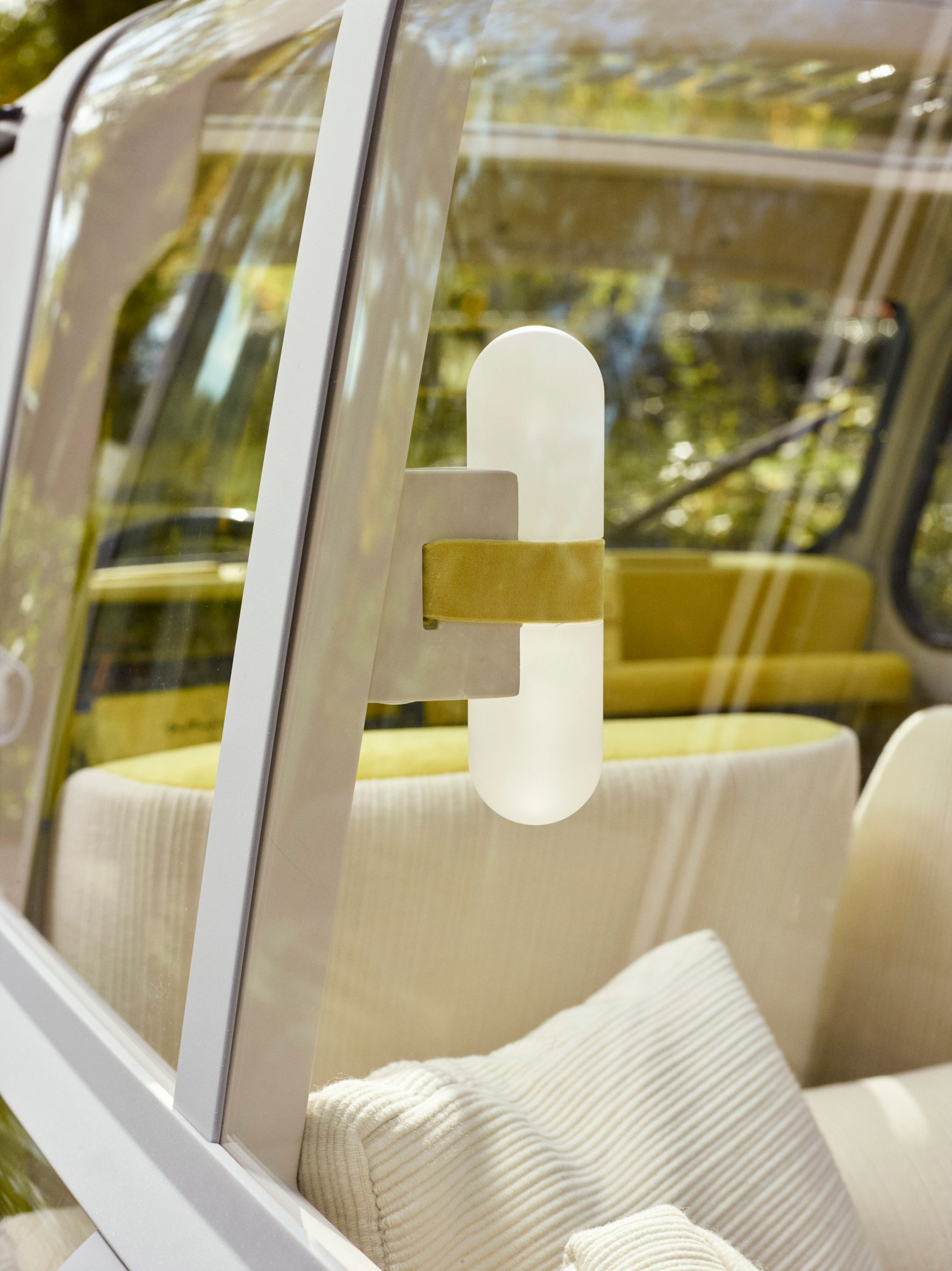  View through the rear windows of the principle automobile revealing cream-coloured cushions and a capsule-shaped wall light