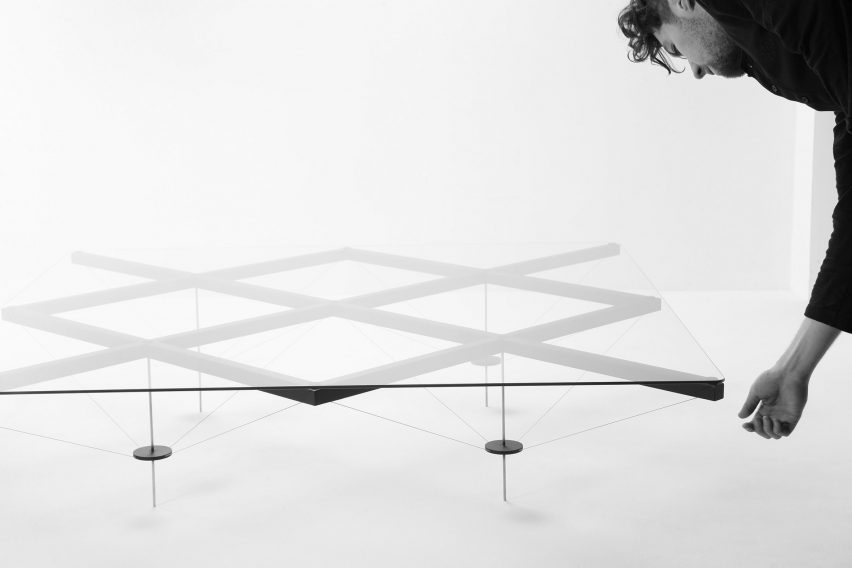 Man leans over a large glass coffee table with a thick metal grid frame beneath it and ultra slender metal legs