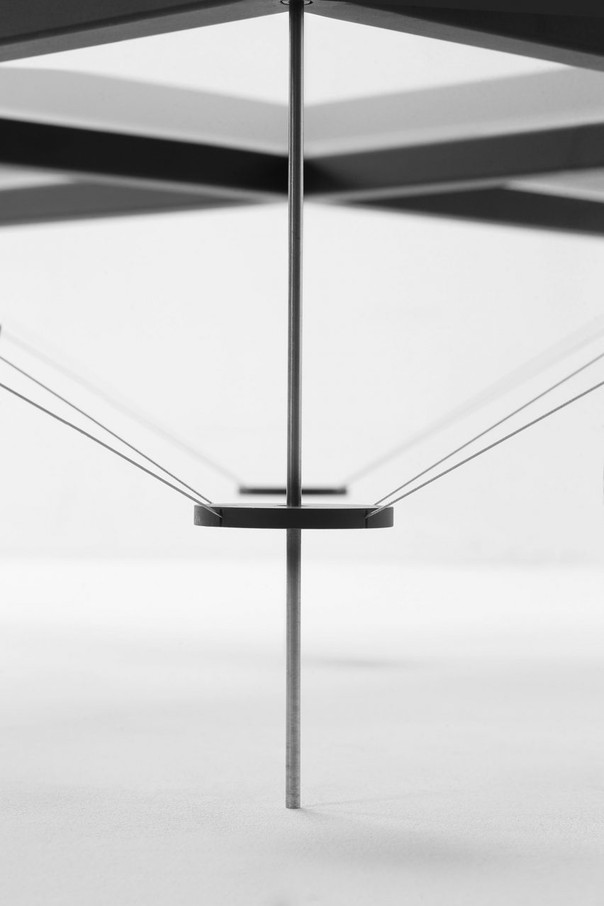Close-up on TT_01 table showing thin metal legs with steel discs halfway up them holding tension cables in place that reach up towards a thick metal structure overhead