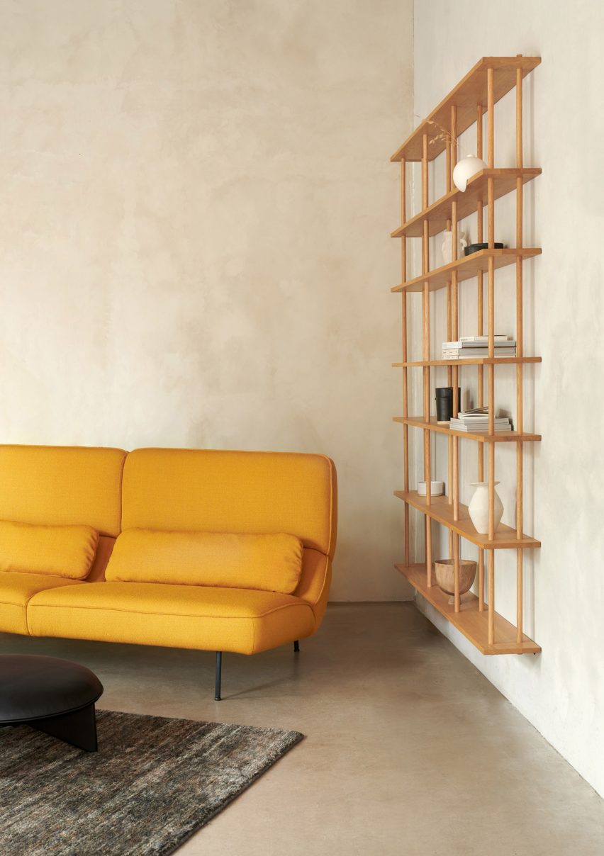 Sofa Velar berwarna kuning di sebelah rak dinding kayu