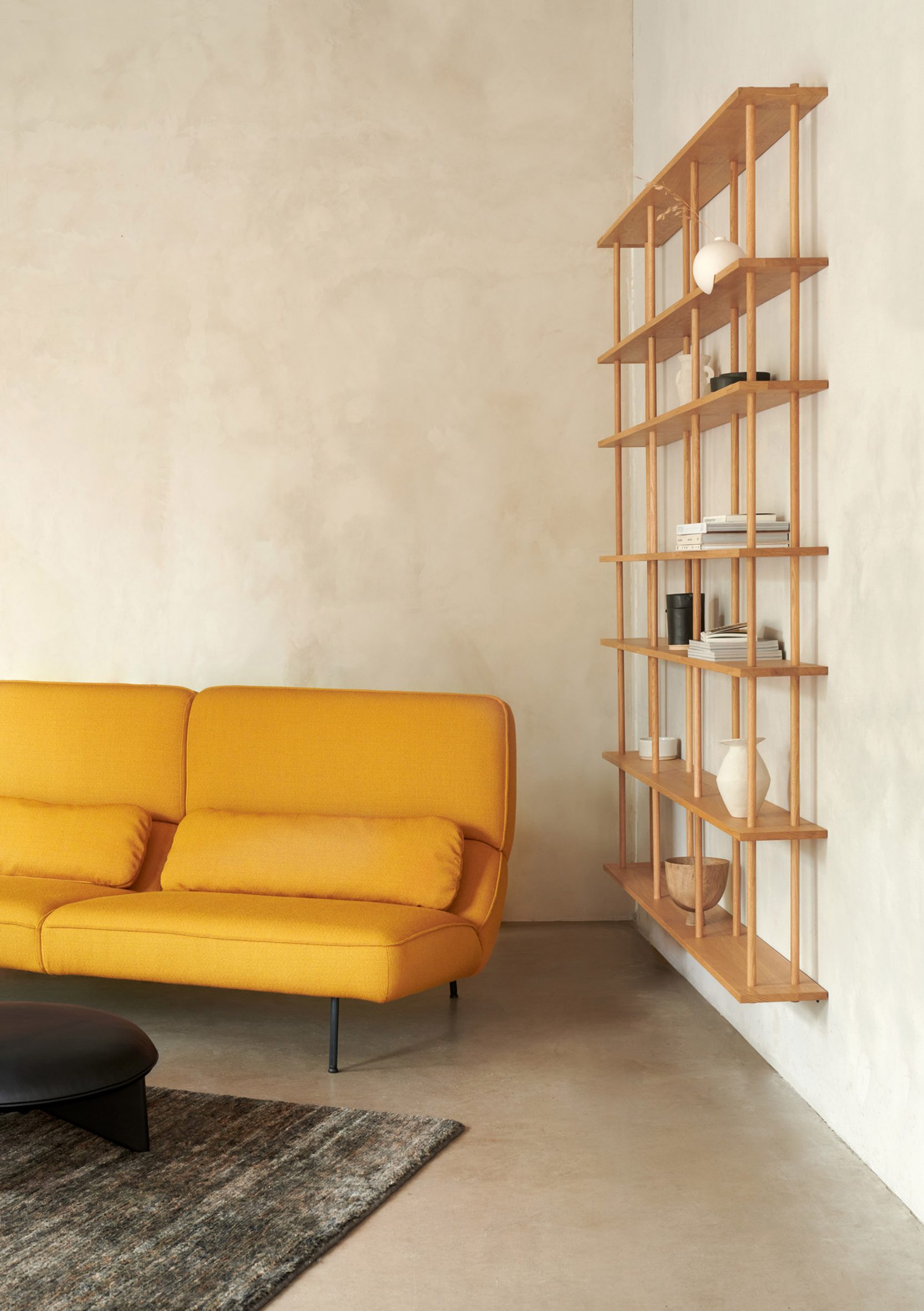Velar sofa in yellow next to a wooden wall shelf