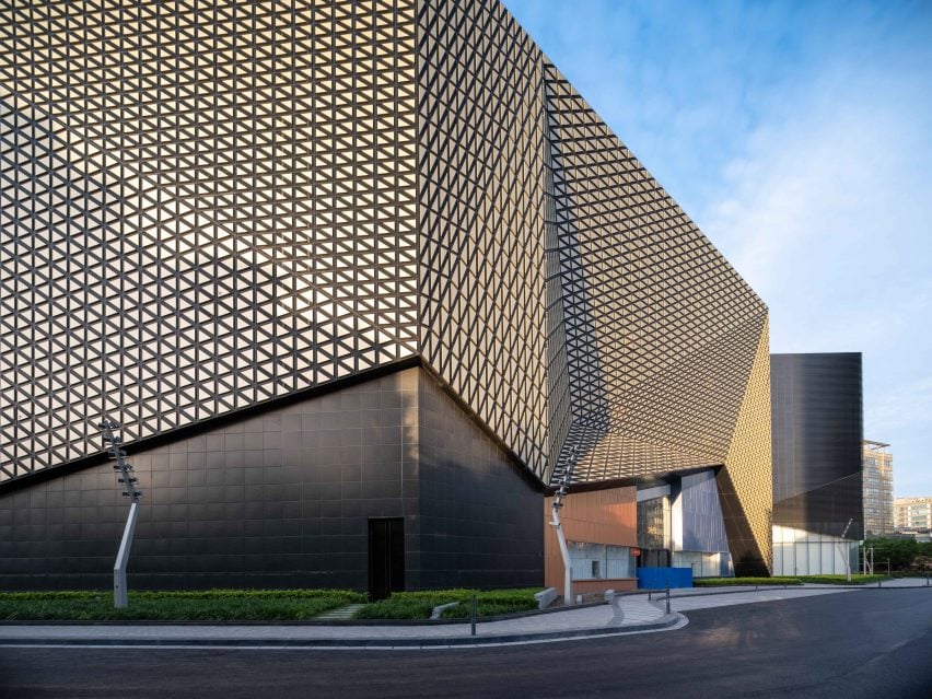 A photograph of the Shanghai Jiuguang Center's west side facade, which is clad with golden triangular blocks