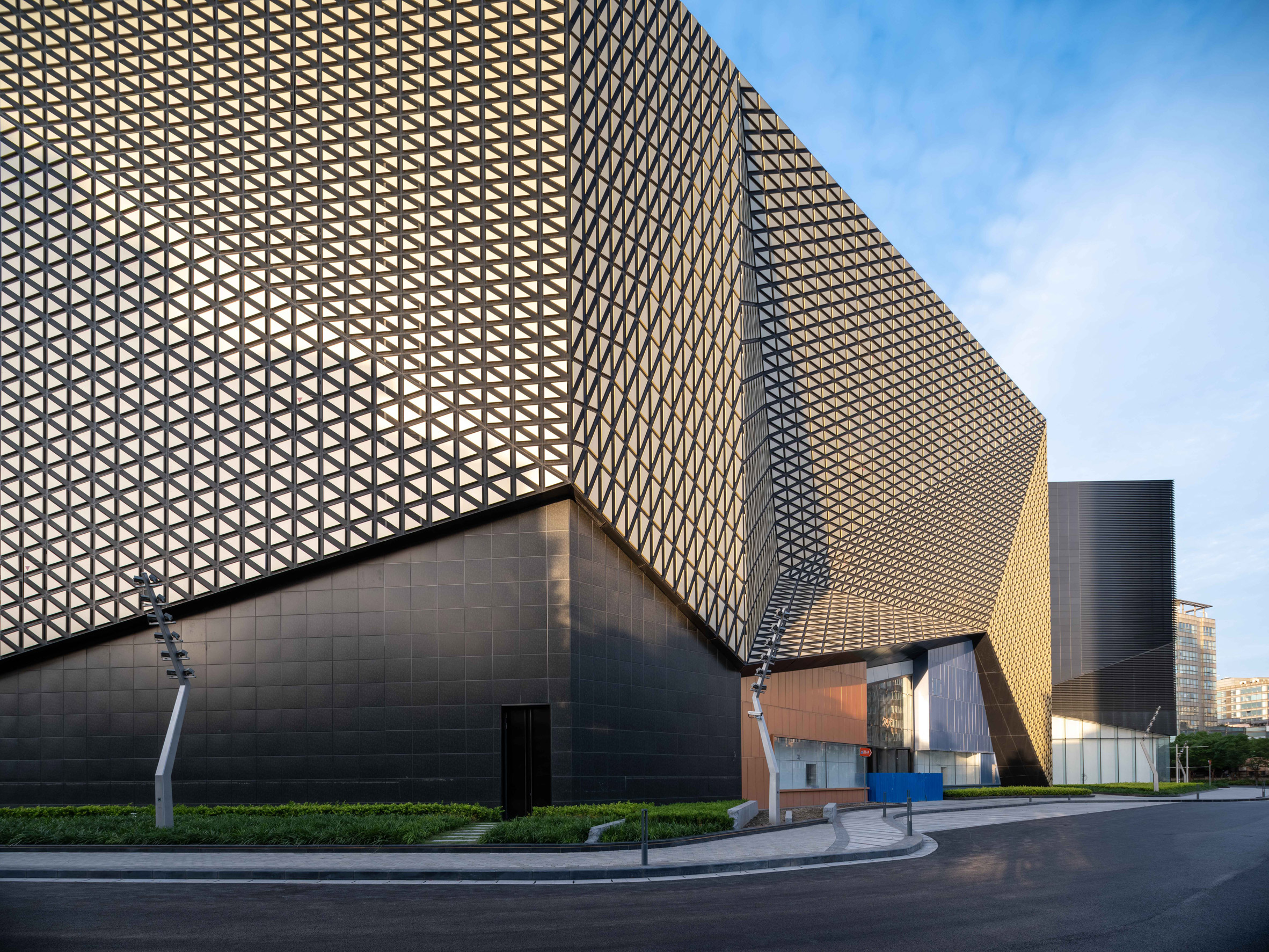 A photograph of the Shanghai Jiuguang Center's west side facade, which is clad with golden triangular blocks