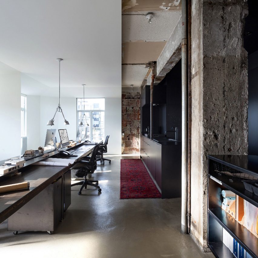 Studio arsitek di Vancouver dengan meja kerja kayu panjang, dapur kecil hitam, dan dinding bata ekspos