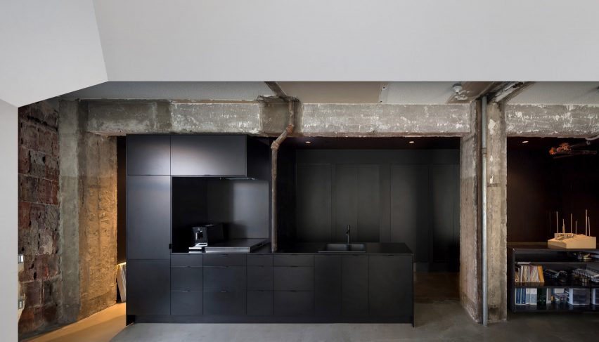 Black kitchenette in Vancouver architecture studio surrounded by rough concrete shell