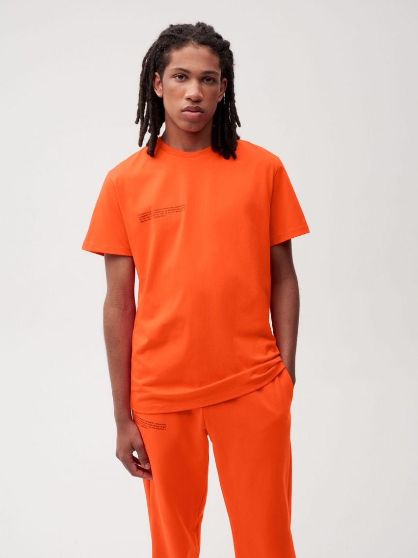 A male model wearing an orange T shirt and jogging pants by Es Devlin