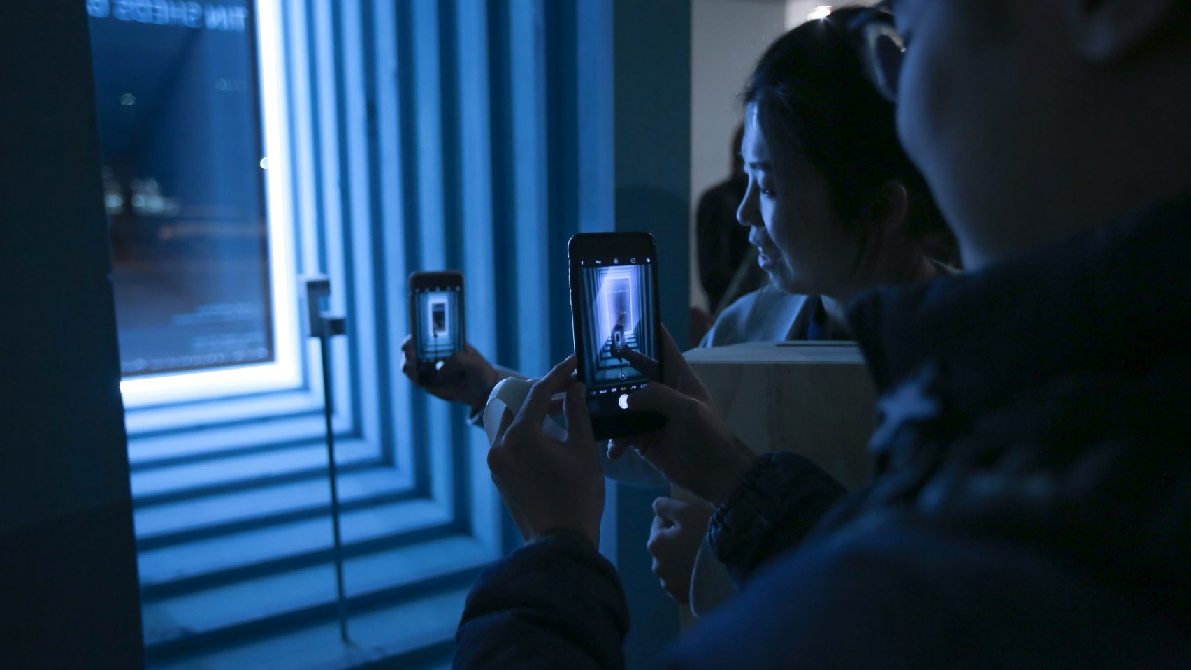 Viewers looking at mobile phones in a blue lightbox