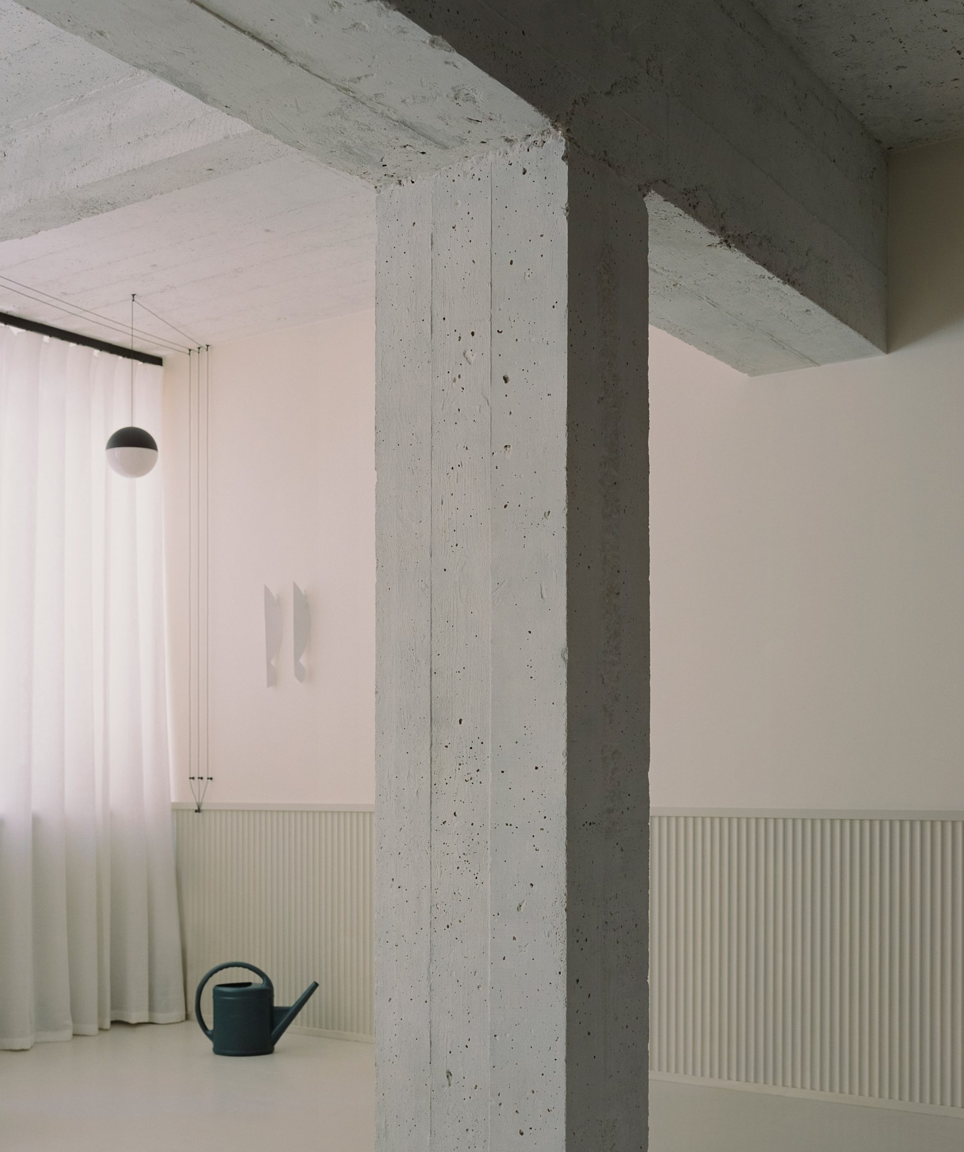 Concrete structural beams and column next to black watering can in The Whale apartment