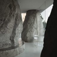 Boulder-like columns surround white chairs and tables in Zolaism Café in Aranya designed by B.L.U.E. Architecture Studio