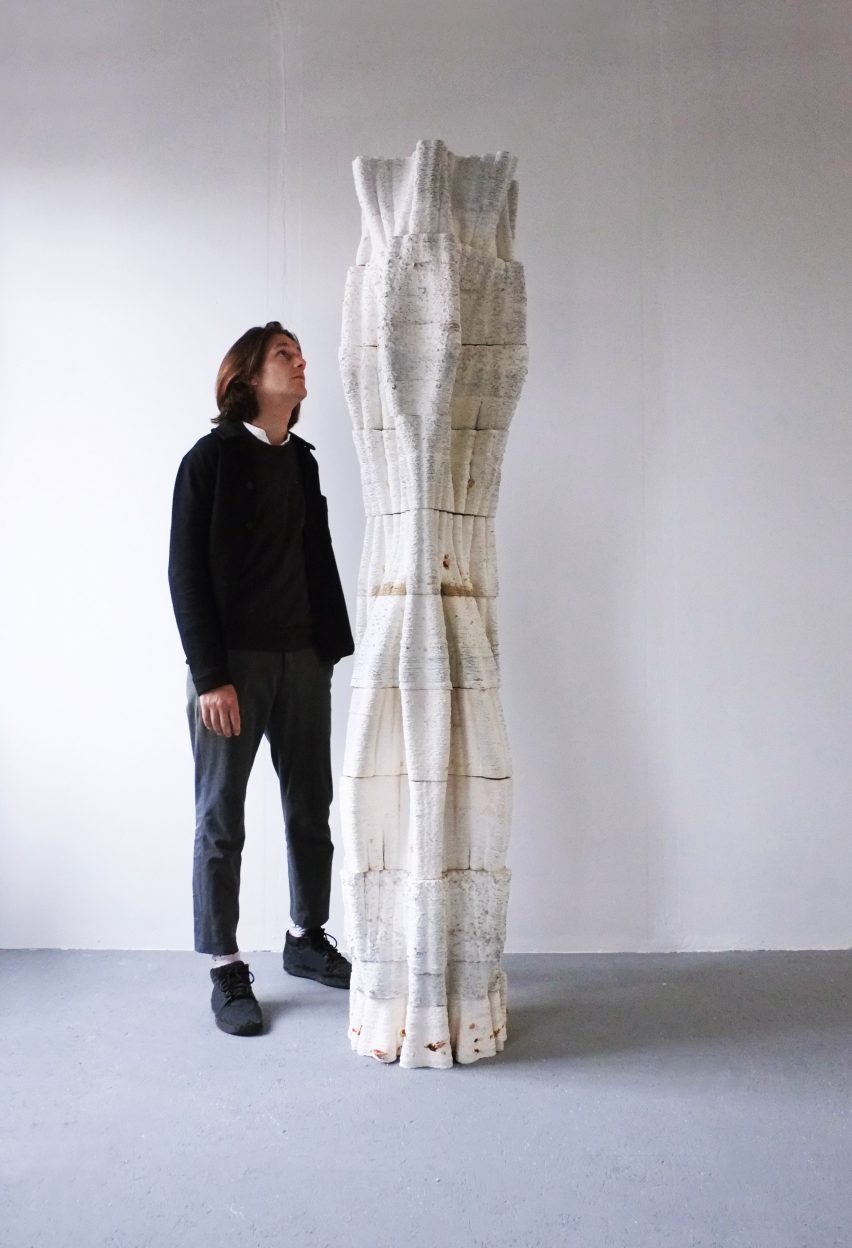Hombre de pie junto a una columna de árbol impresa en 3D a partir de micelio que se eleva sobre él