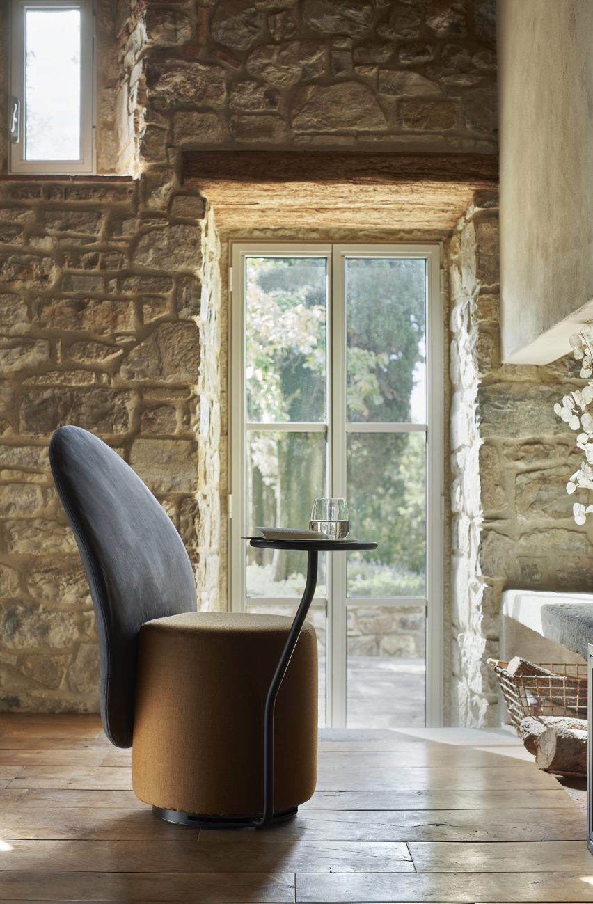 Loomi armchair in a space with stone walls and wood floors, with the optional swivel table holding a glass and notebook