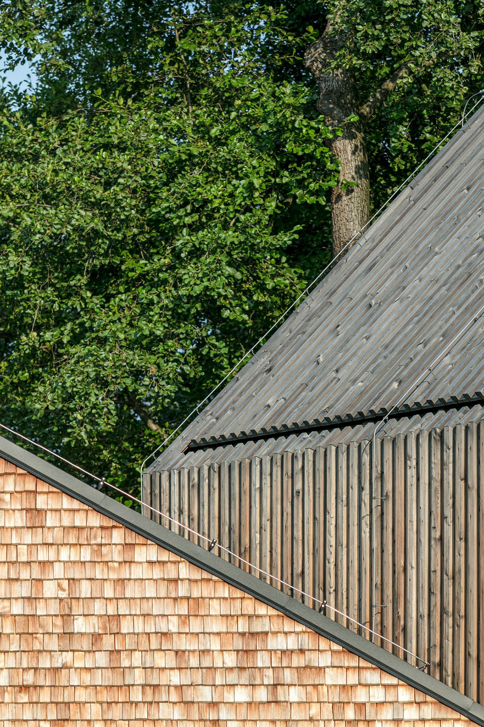 Intersecting roofs on a wooden building, one part clad in square shingle-like elements and one with planks
