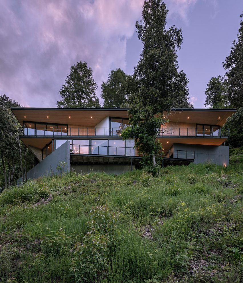 A house with vast windows on top of a grassy hill