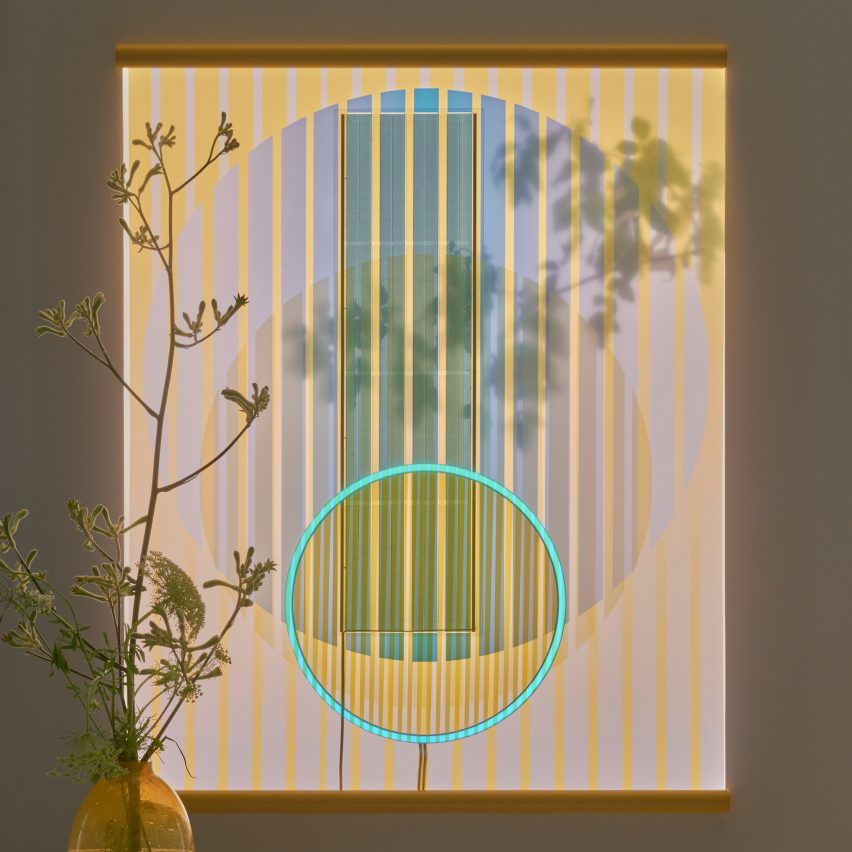 Ra tapestry made from solar cells by Marjan van Aubel pictured hung behind a vase with flowers and shown at dusk with glowing blue ring at the centre