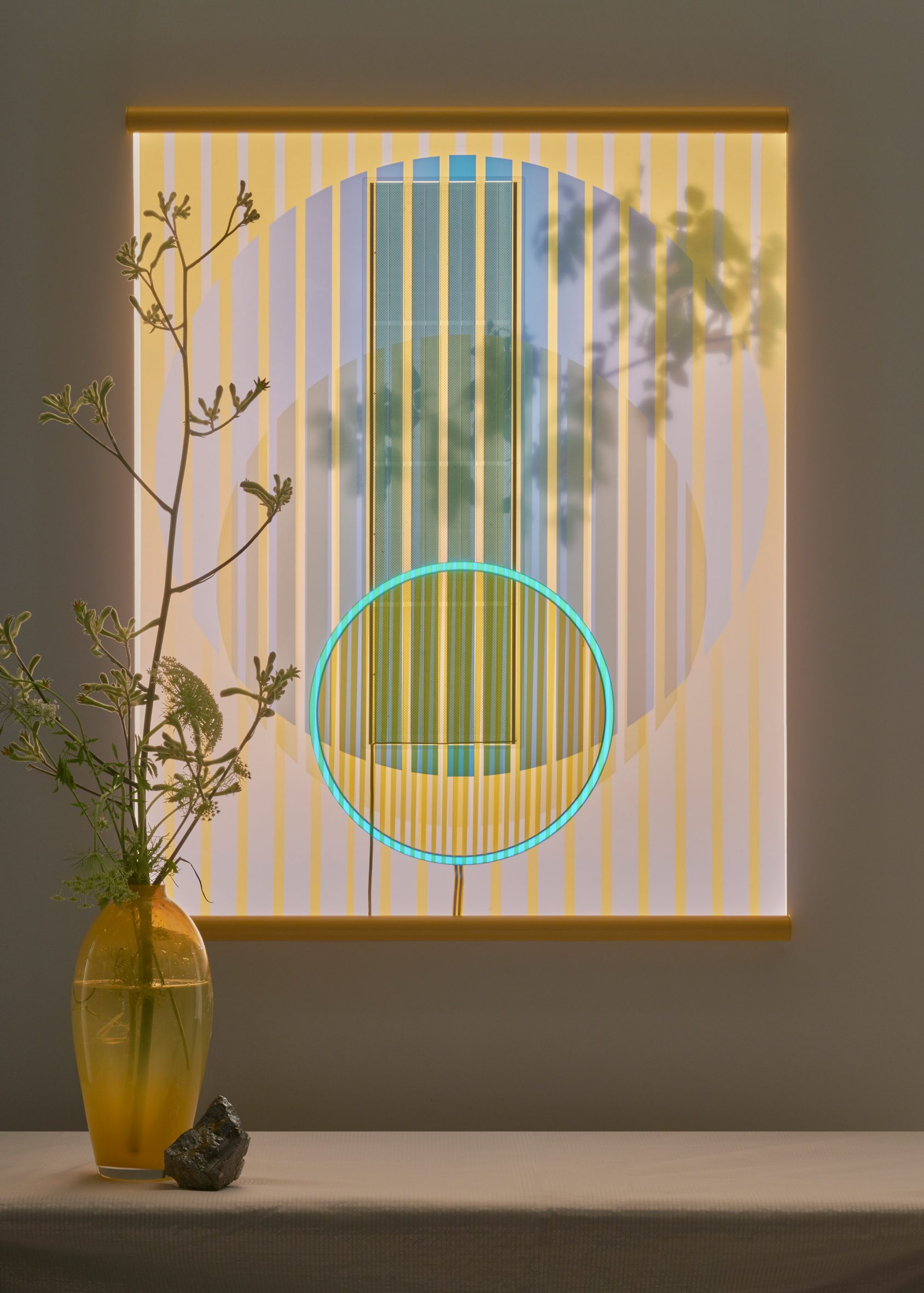 Wallhanging made from solar panels by Marjan van Aubel pictured at dusk, hung behind a vase with flowers