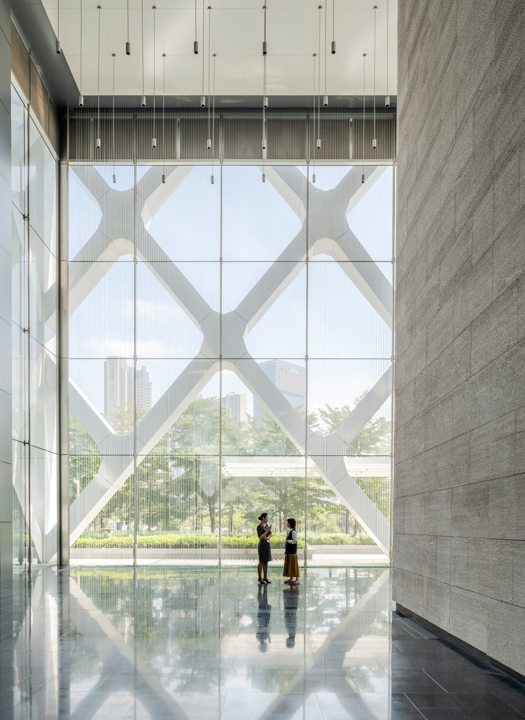 Lobby of SOM's Shenzhen bank building with stone-clad walls on one side and rain-curtain feature in the foreground and exterior diagrid structure visible behind it