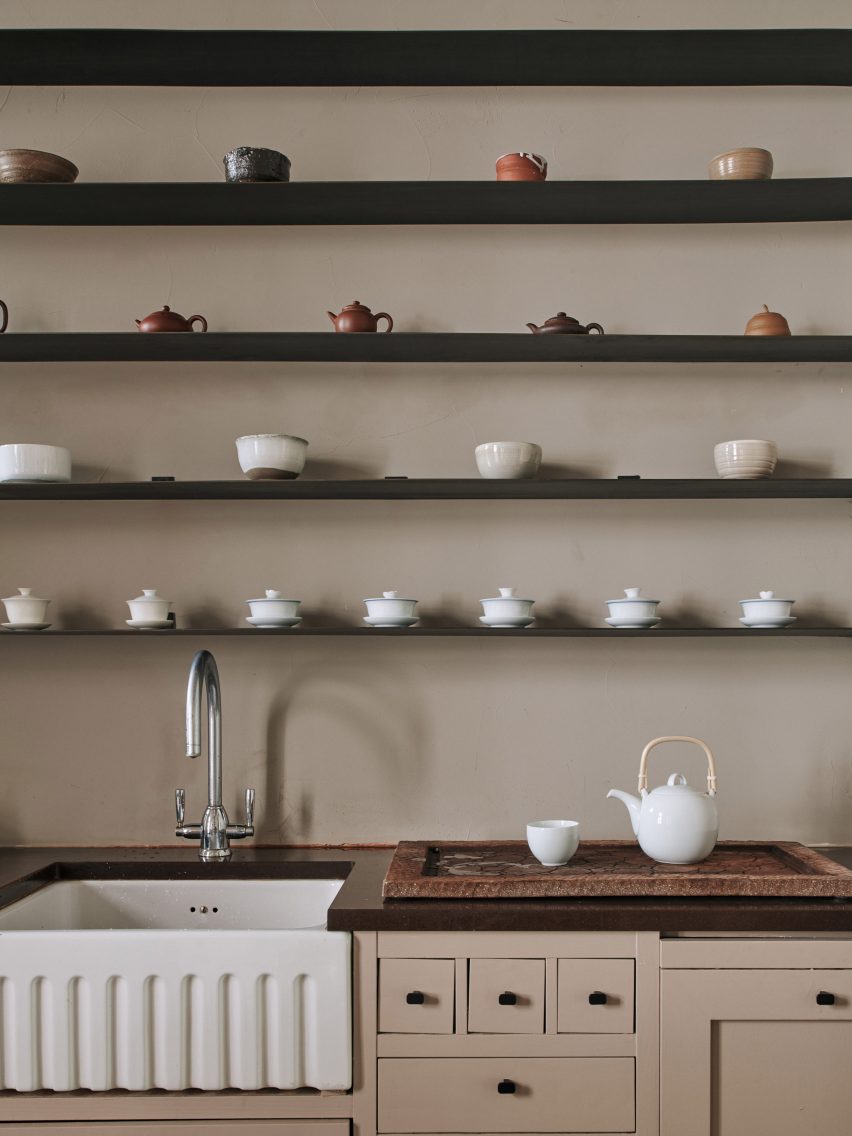 Teapots and cups in different colours displayed on black shelves above a kitchen sink in Helsinki teahouse designed by Yatofu