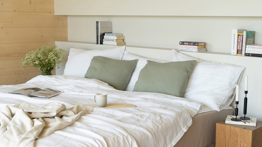 A bed with white sheets and green pillows backed onto a wall painted in a light green Teknos paint and side wall exposed timber