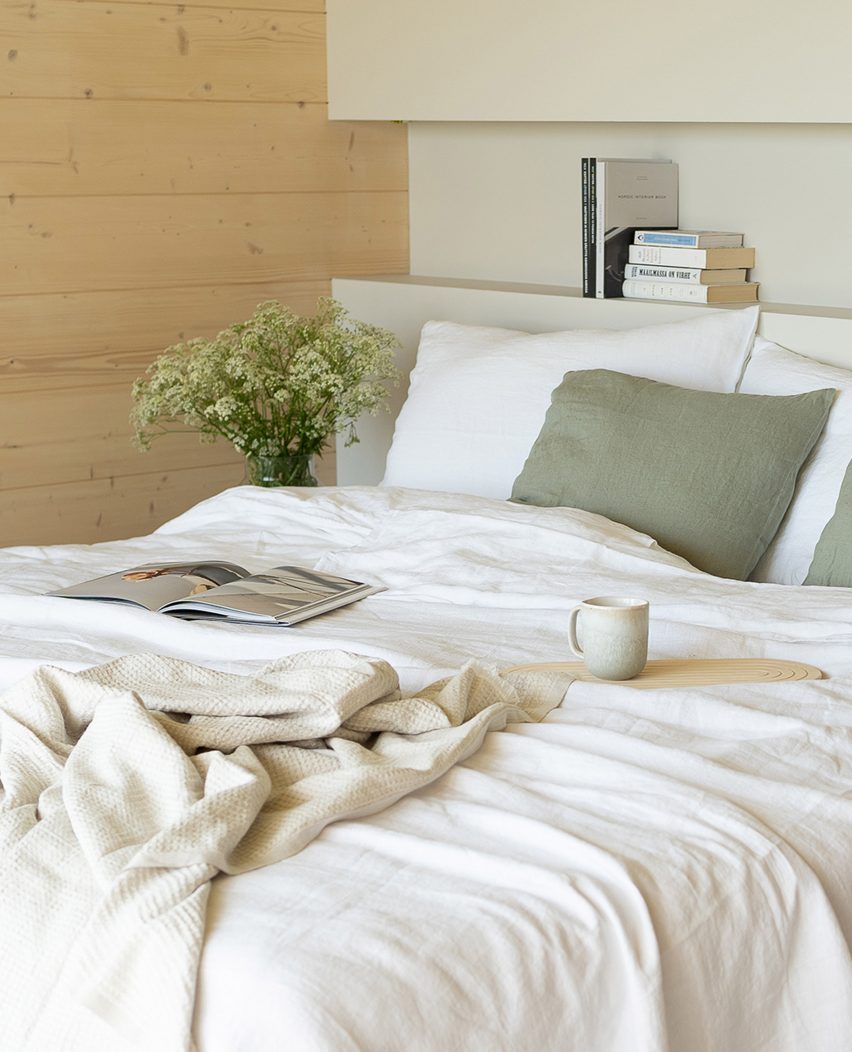 Bed with white sheets and green pillows with the back wall painted in a light green Teknos paint and side wall clad with timber.