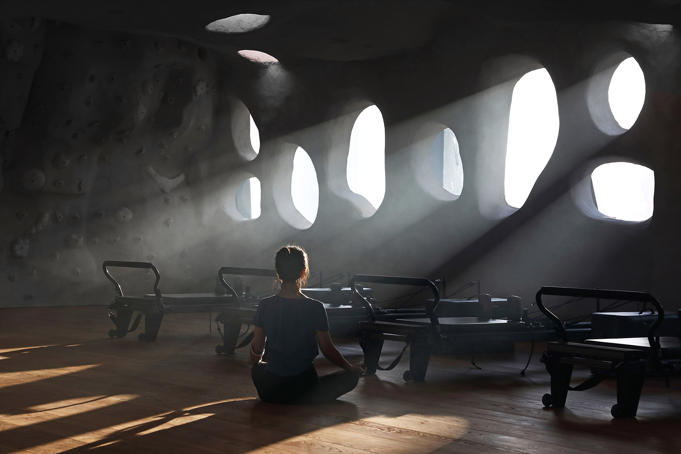 Woman sitting crosslegged on floor of T.T. Pilates studio in Xiamen by Wanmu Shazi with light streaming in through rounded windows