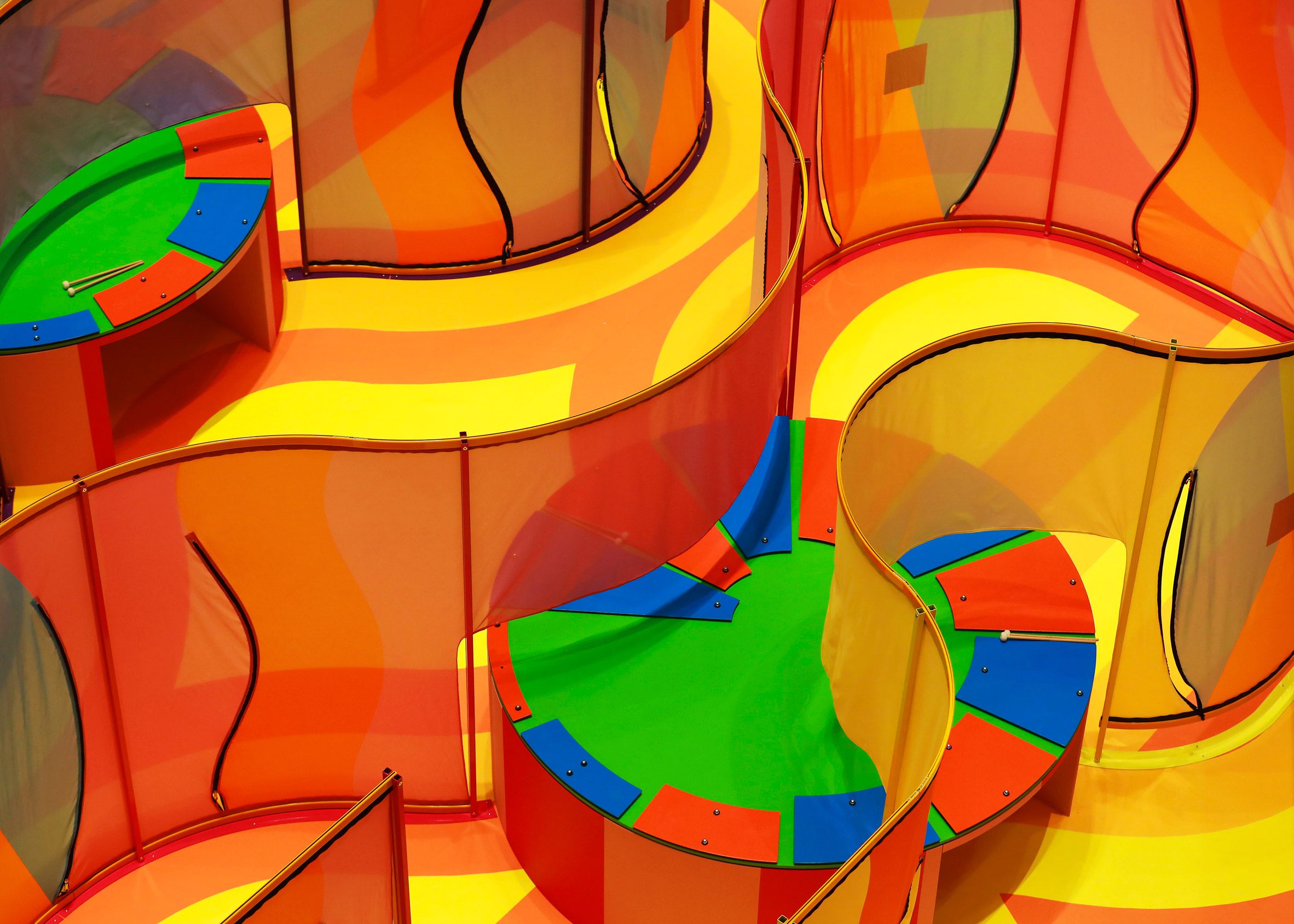 Two large and colourful circular xylophones embedded within waved mesh maze walls in the Listening to Joy installation