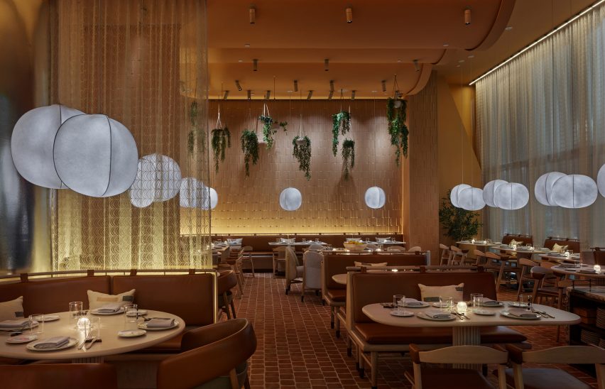 Terracotta-tiled dining room of New York restaurant designed by Rockwell Group with leather-upholstered seating booths separated by sheer curtains and illuminated by lantern-style lights