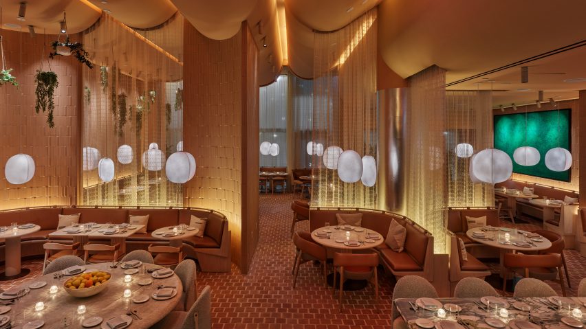 Terracotta-tiled dining room of New York's Casa Dani restaurant designed by Rockwell Group with leather-upholstered seating booths separated by sheer curtains and illuminated by lantern-style lights