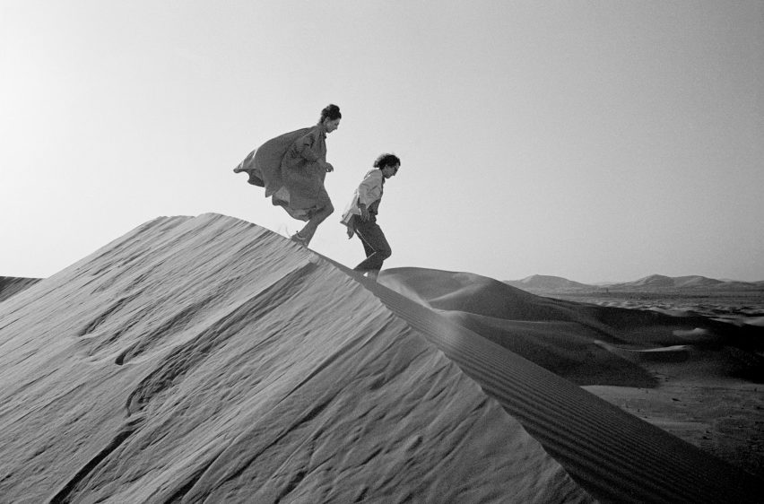Black-and-white photograph of Christo and Jeanne-Claude walking over sand dunes in a desert