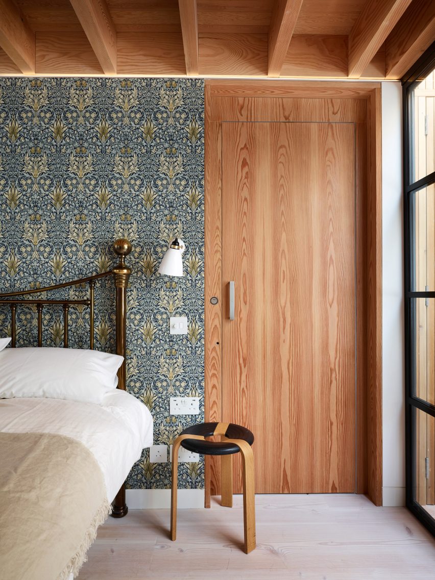Bedroom interior of Danish Mews House by Neil Dusheiko Architects with wooden doors and chintzy wallpaper